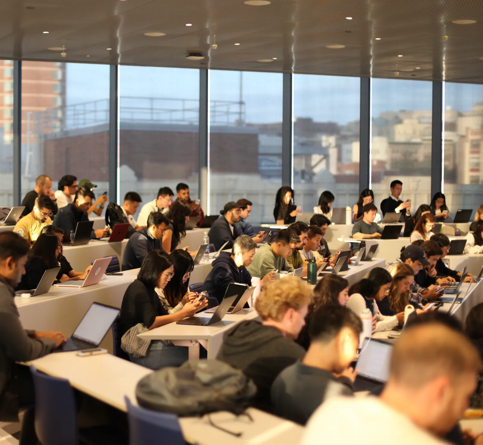 Students working on laptops in a sunlit classroom.