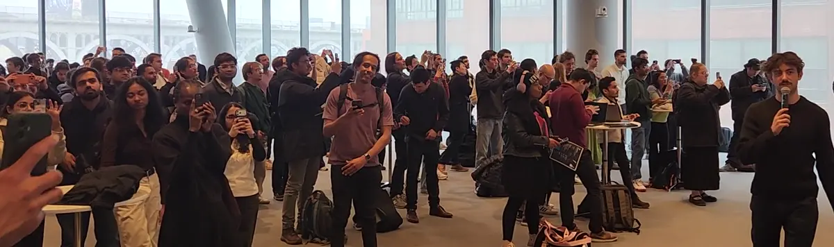 A crowd gathered in a bright glass walled room.